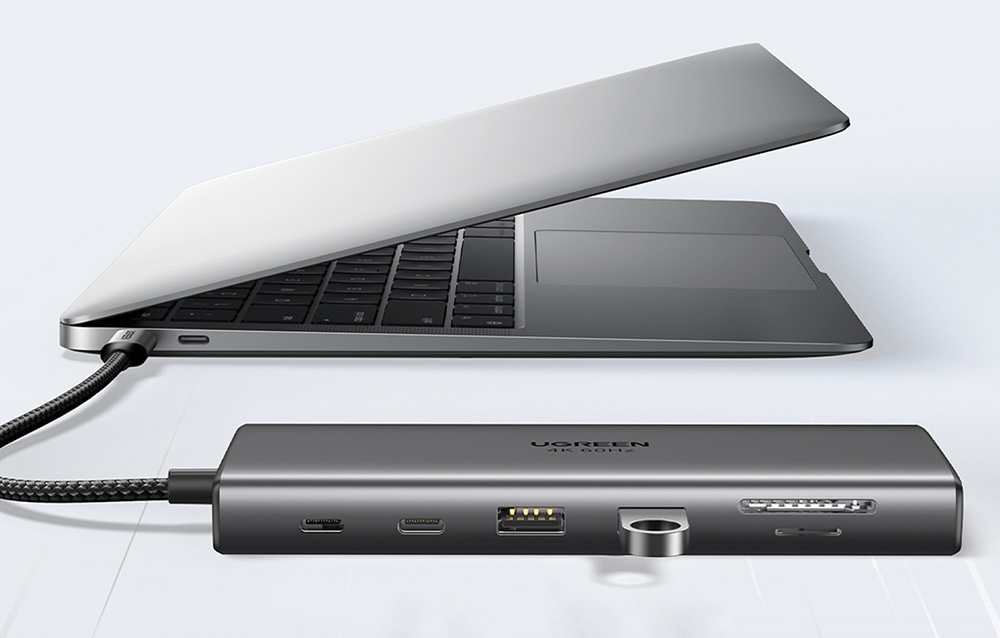 Srebrny hub z podłączonym pendrivem podpięty do laptopa na szarym tle