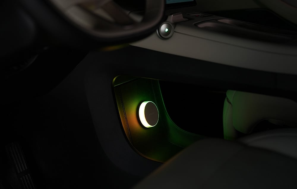 Lampka nocna Yeelight Vega zamontowana w dolnej części deski rozdzielczej samochodu, świecąca zielono-żółtym światłem.