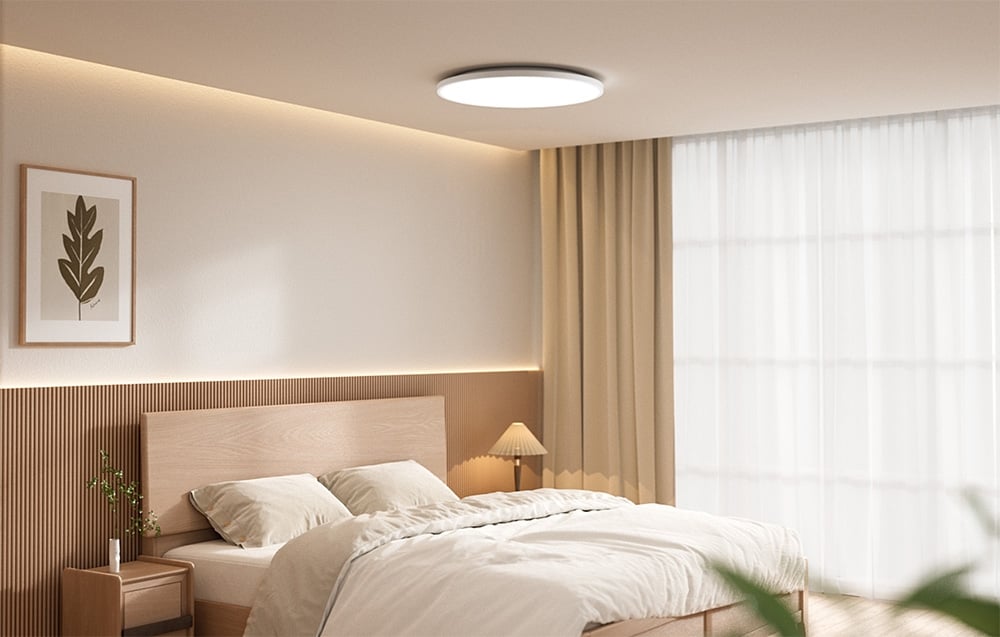 Jasna sypialnia z łóżkiem i włączoną lampą sufitową Yeelight Mercury C300 zamontowaną na suficie.