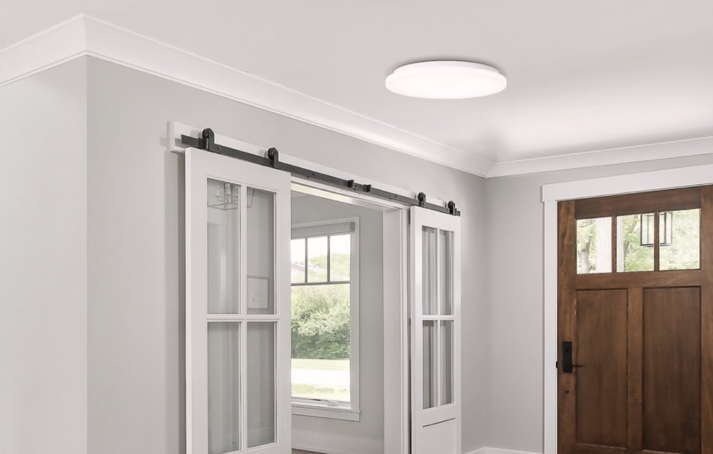 Lampa Yeelight MercuryE C260 zamontowana w jasnym holu z przesuwanymi drzwiami i drewnianymi drzwiami wejściowymi.