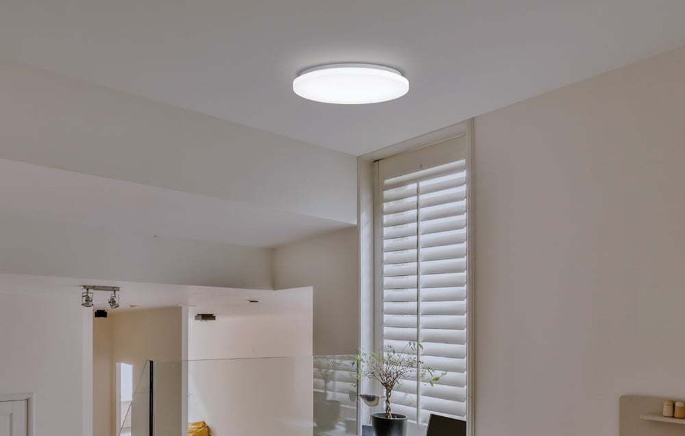 Lampa Yeelight MercuryE C260 zamontowana we wnętrzu z żaluzjami pionowymi i doniczką na parapecie.