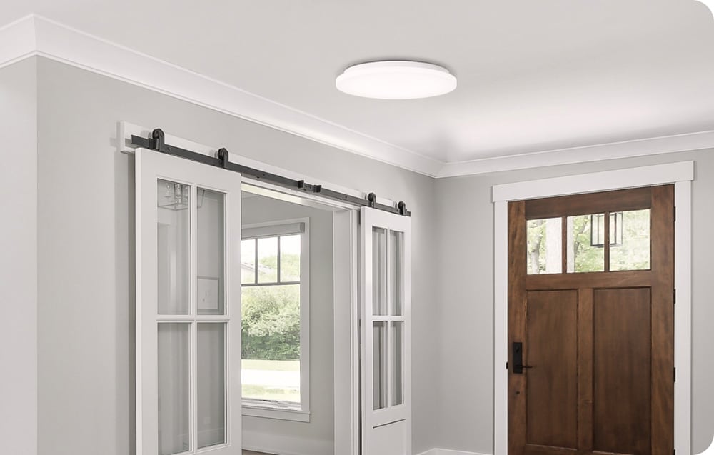 Lampa Yeelight MercuryE C300 zamontowana w jasnym holu z przesuwanymi drzwiami i drewnianymi drzwiami wejściowymi.