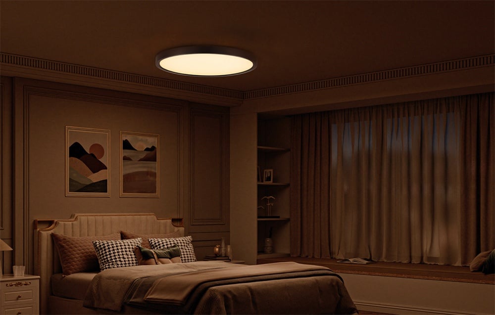 Lampa sufitowa Yeelight Meteor C300 świecąca w przyciemnionej sypialni z beżową pościelą i obrazami nad łóżkiem.