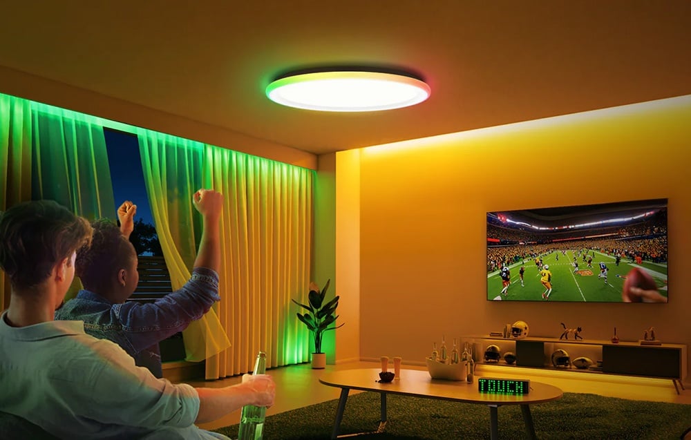 Dwóch mężczyzn oglądających mecz w salonie oświetlonym lampą Yeelight Mars C400 w kolorze zielonym i żółtym.