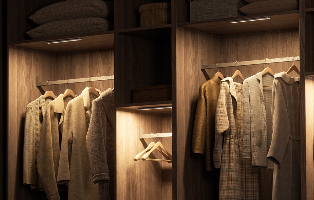 Lampki do szafy Yeelight zamontowane w górnej części drewnianej garderoby oświetlające ubrania na wieszakach.