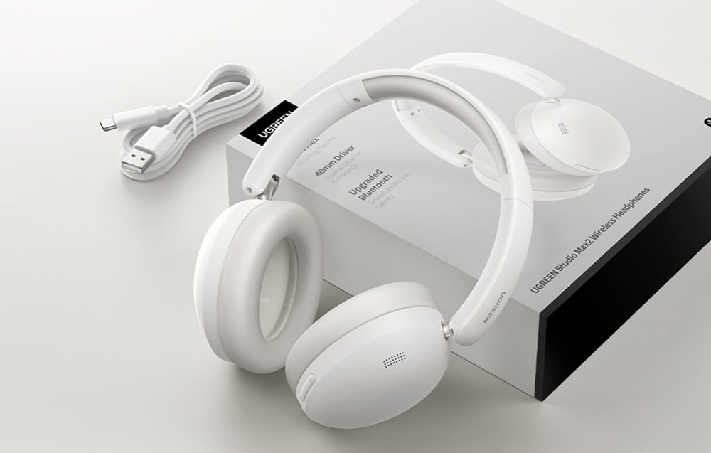 białe słuchawki Ugreen Studio Max2 oparte o opakowanie, obok którego leży kabel ładujący