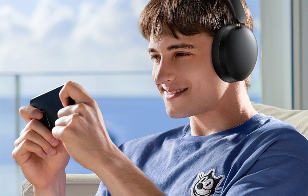 mężczyzna w niebieskiej koszulce grający w grę mobilną, noszący słuchawki Ugreen Studio Max2
