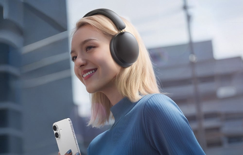 kobieta w niebieskim golfie słuchająca muzyki przez słuchawki Ugreen Studio Max2, w tle znajdują się budynki miejskie 