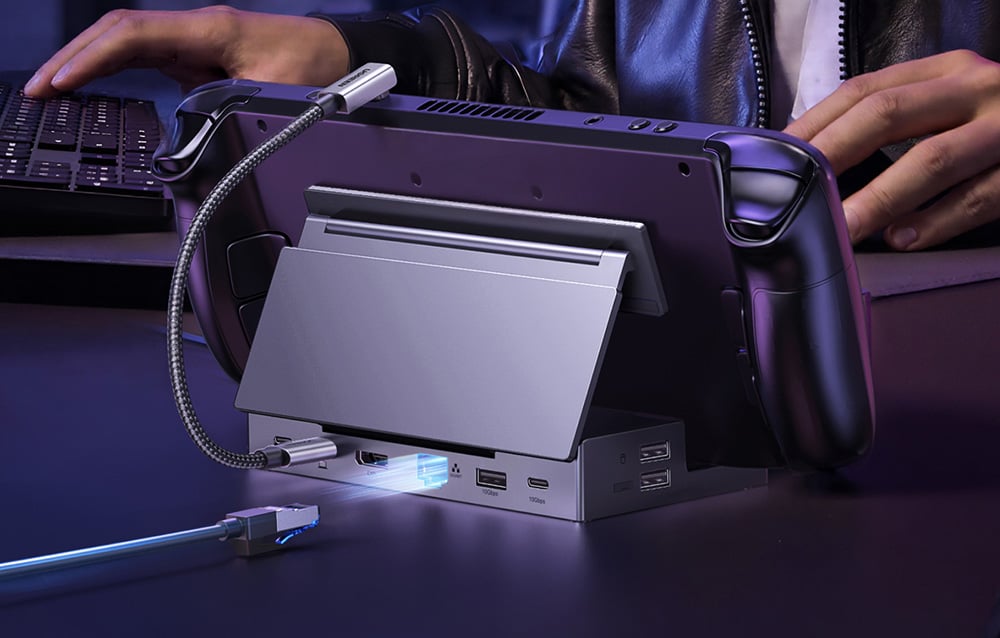 Adapter Ugreen CM800, na którym leży przenośna konsola do gier, w tle osoba korzysta z klawiatury.