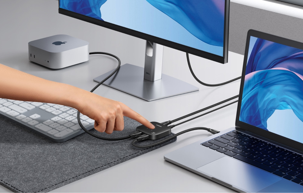 Osoba naciskająca na przełącznik Ugreen AW700, który podłączony jest do laptopa, routera i monitora.