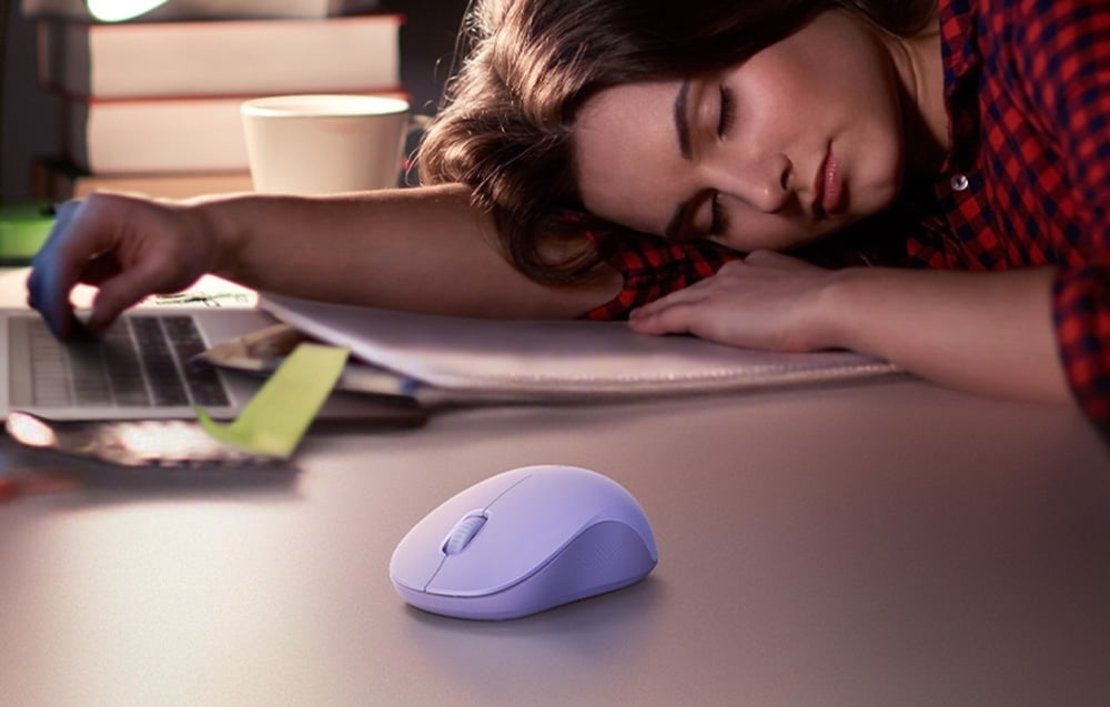 Kobieta w czerwonej koszuli w kratę drzemiąca przed laptopem, na froncie znajduje się mysz Ugreen M331 w fioletowym kolorze.