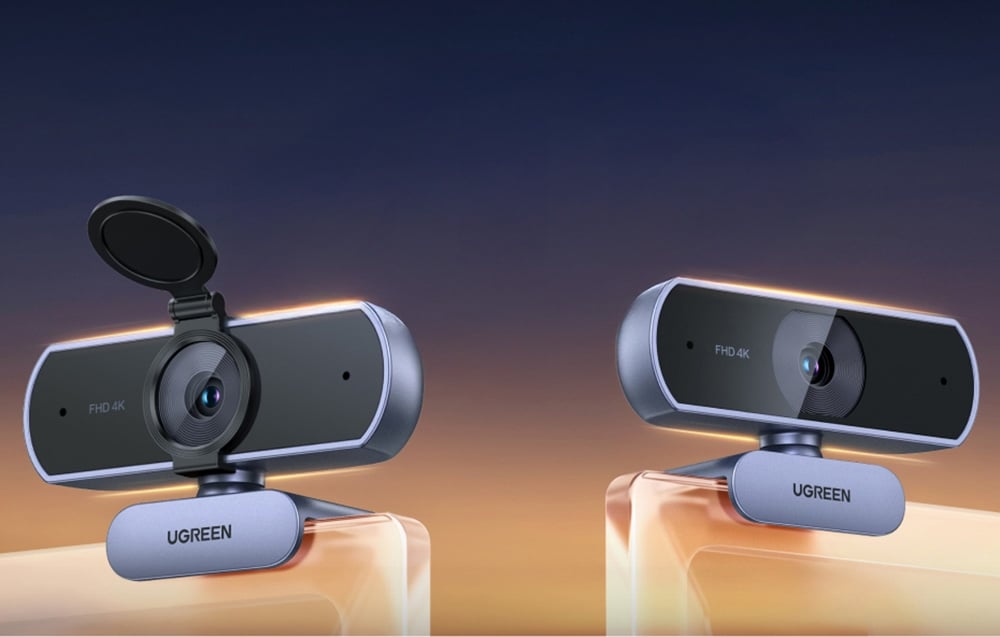 Zbliżenie na dwie kamery internetowe Ugreen CM831 stojące obok siebie na granatowo-pomarańczowym tle.