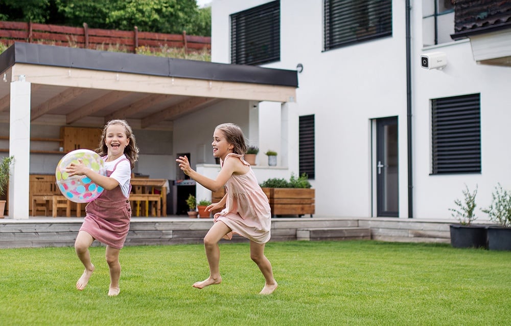 Dwie dziewczynki grające w piłkę na trawniku przed nowoczesnym domem z tarasem i czarnymi żaluzjami