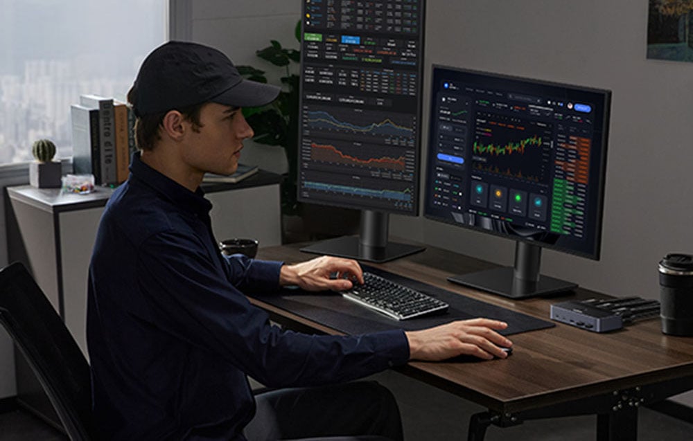 A young man sitting in front of a computer. On the monitors, there is audio editing software.