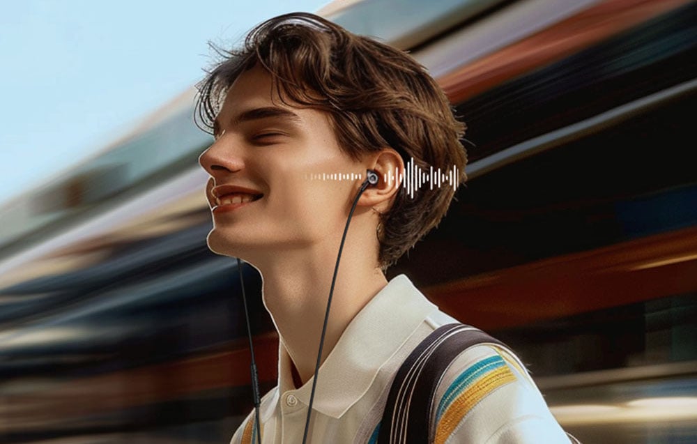 A smiling man in wired headphones stands against the backdrop of a passing train with a visualization of sound waves
