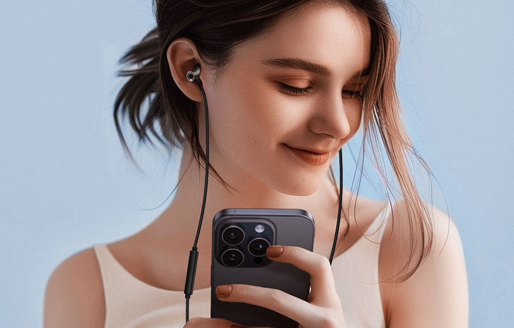 A woman in a light top listens to music on wired in-ear headphones while holding a smartphone
