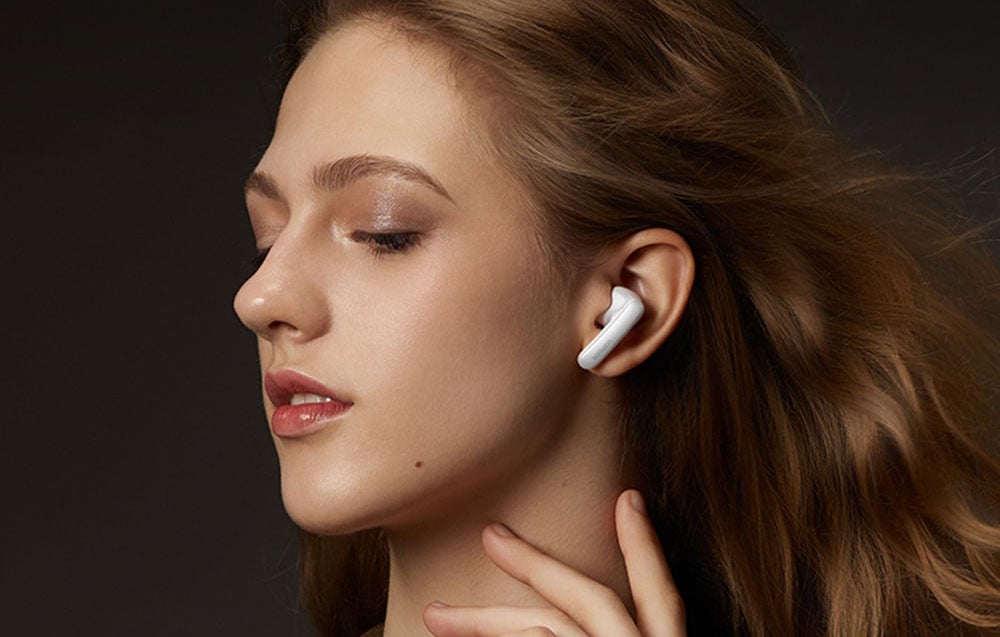 Kobieta z długimi włosami nosi białą bezprzewodową słuchawkę douszną na ciemnym tle