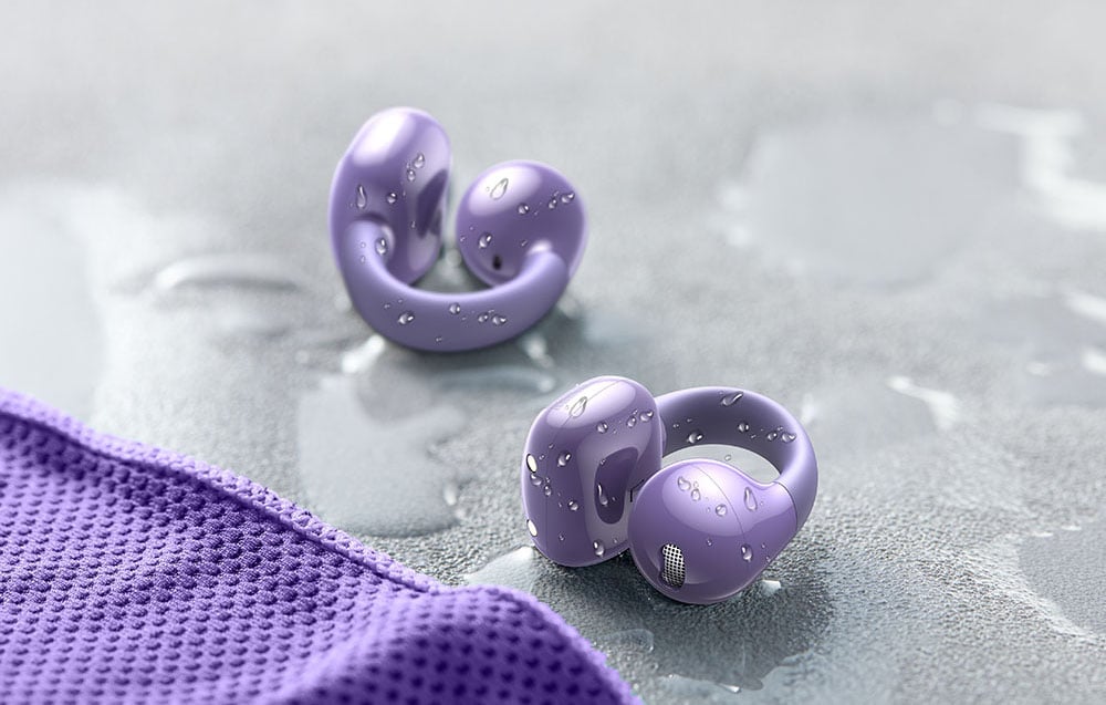 Two purple wireless headphones covered with water droplets lying on a wet surface next to a purple cloth