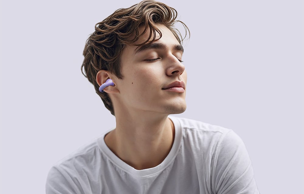 A man in a white shirt with closed eyes is wearing a purple wireless in-ear headphone