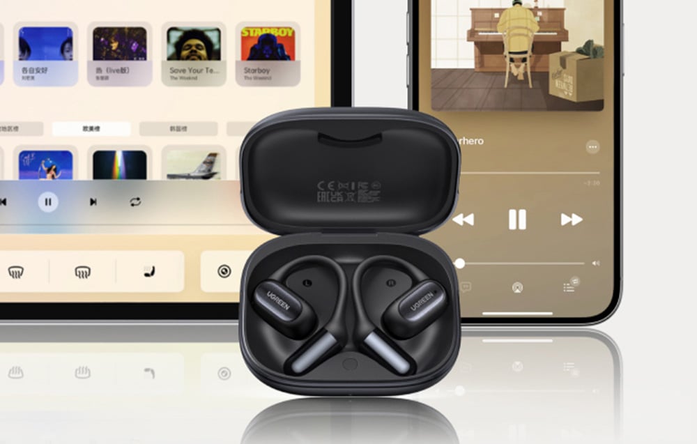 Czarne słuchawki bezprzewodowe w etui stojące przed tabletem i smartfonem z włączonymi aplikacjami muzycznymi