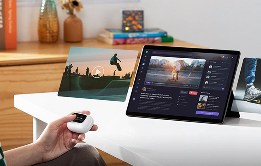 Osoba trzyma etui ze słuchawkami przed tabletem, na którym odtwarzane są treści multimedialne