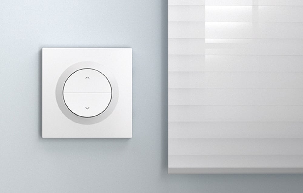 White switch on a light wall. To the right, a white roller blind.