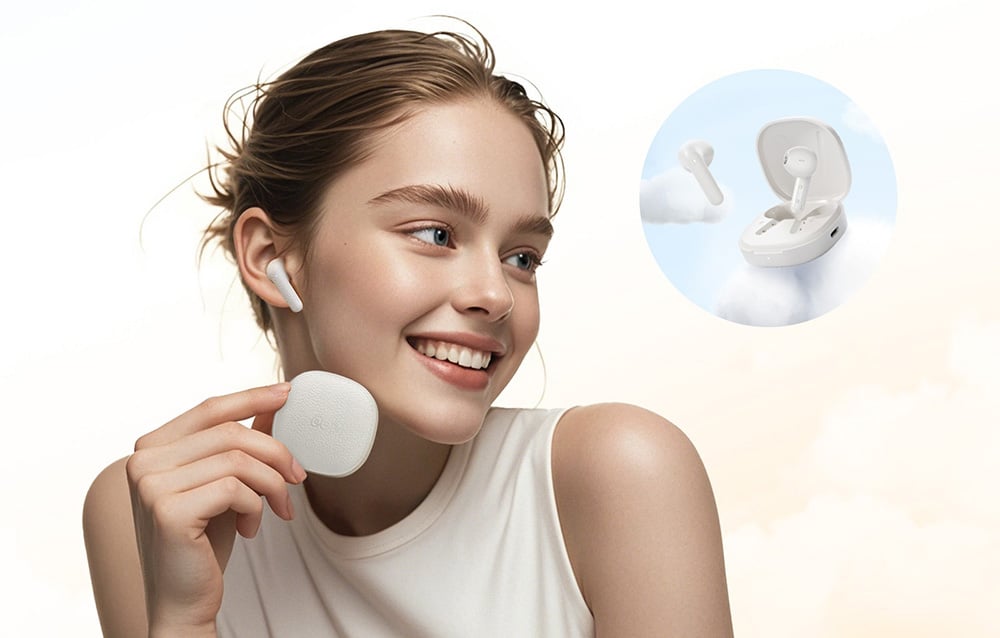 A young, smiling woman with tied hair holding a charging case in her hand. She has a headphone in her ear.