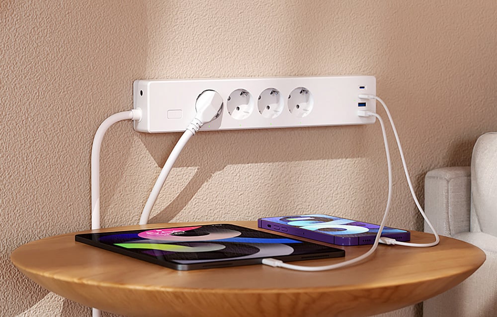 Biała listwa zasilająca z trzema podłączonymi urządzeniami leżącymi na okrągłym stoliku, w tym telefonem i tabletem