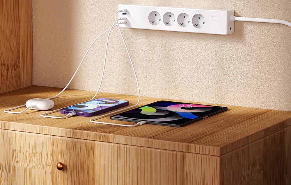 Listwa zasilająca z podłączonymi słuchawkami, smartfonem i tabletem, leżącymi na blacie z jasnego drewna