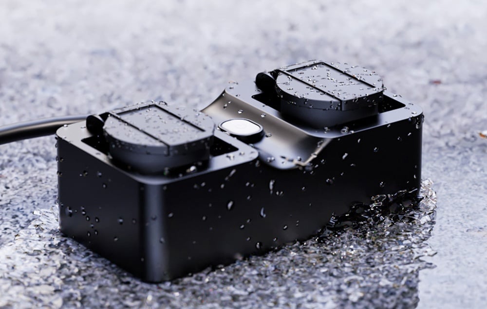 Black waterproof power strip with two sockets, lying on a wet surface with water droplets