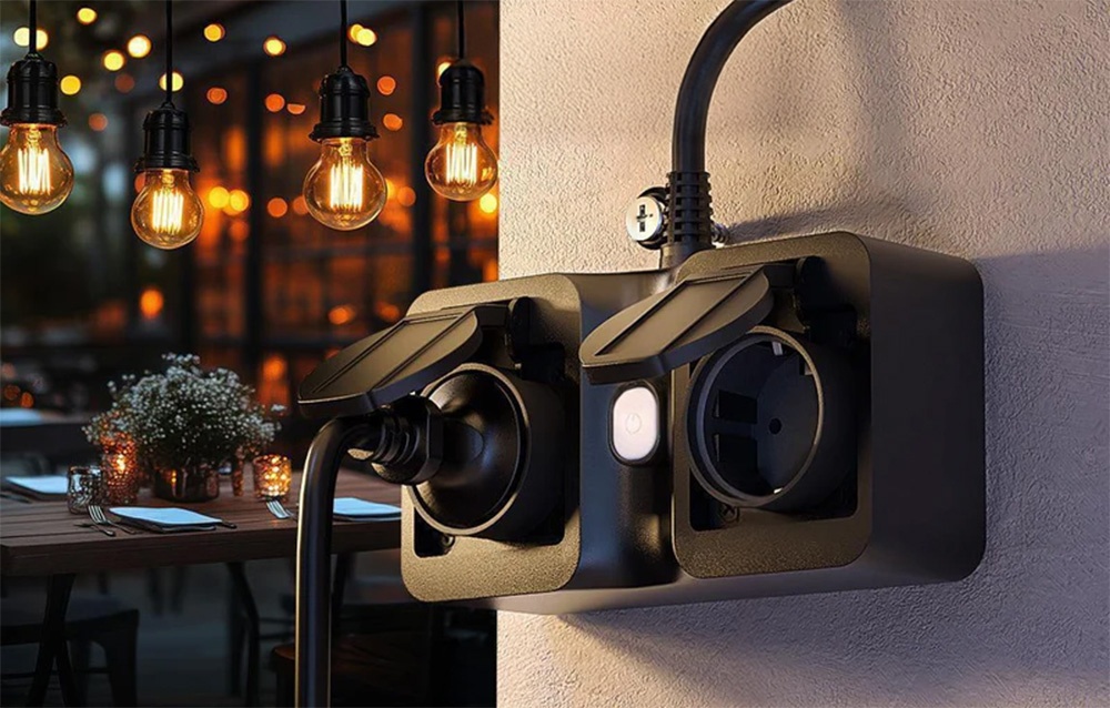 Double outdoor socket with one connected cable, mounted on a wall near a lit terrace