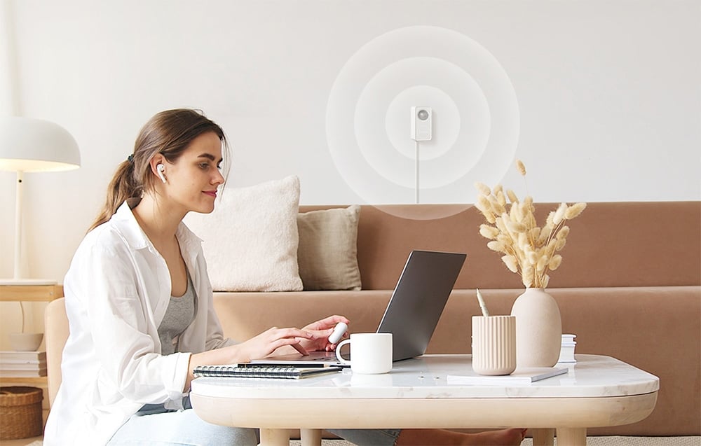 Kobieta pracująca przy laptopie, a w tle na ścianie widoczny czujnik ruchu z graficzną reprezentacją sygnału