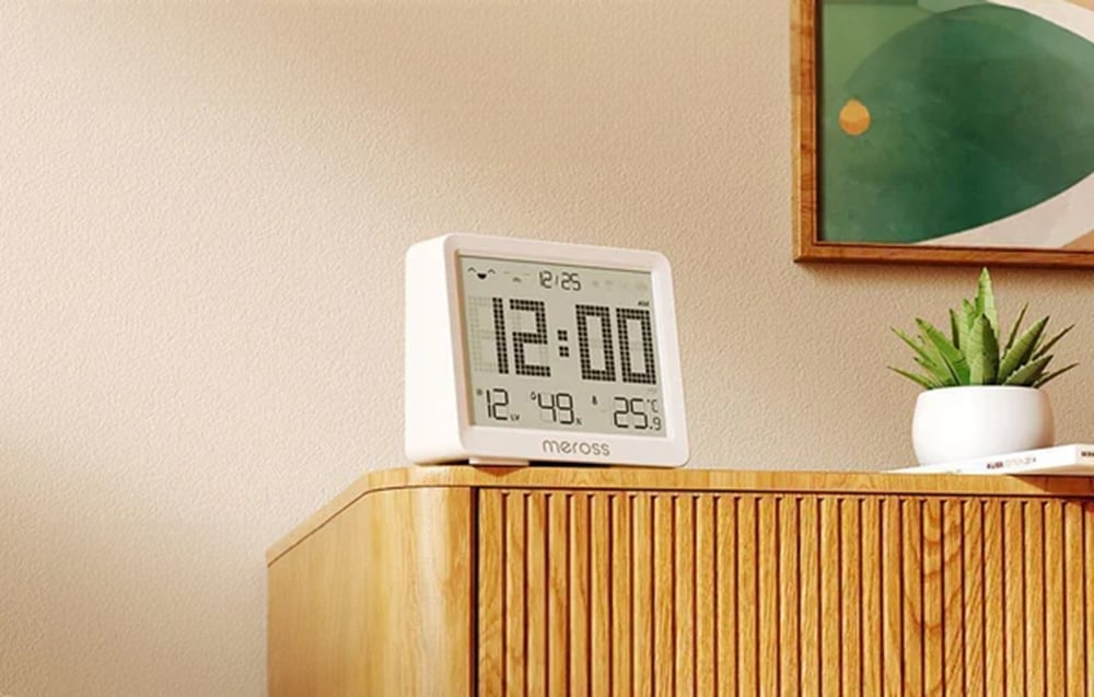 Cyfrowy zegar Meross z wyświetlaczem godziny, temperatury i wilgotności, stojący na drewnianej komodzie