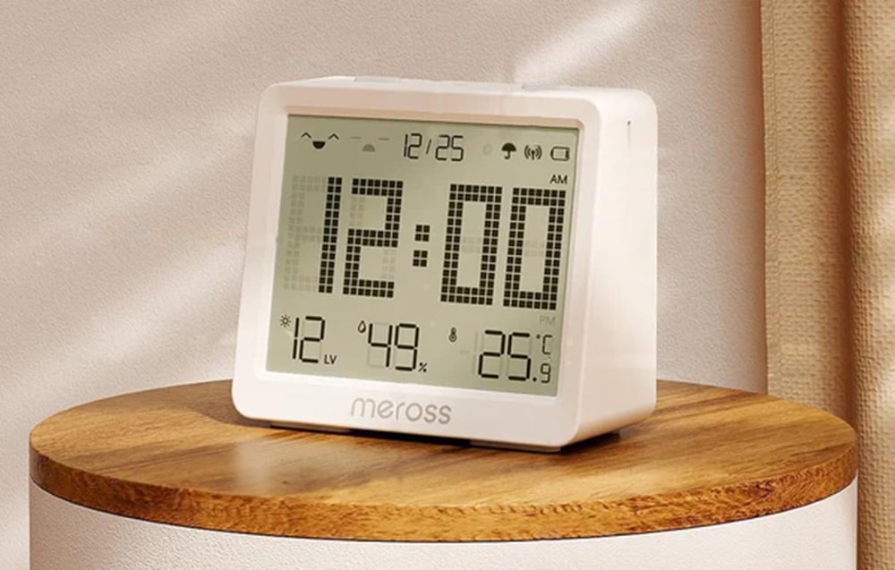 Zegar Meross z dużym cyfrowym wyświetlaczem, pokazujący godzinę, temperaturę i wilgotność, ustawiony na okrągłym stoliku
