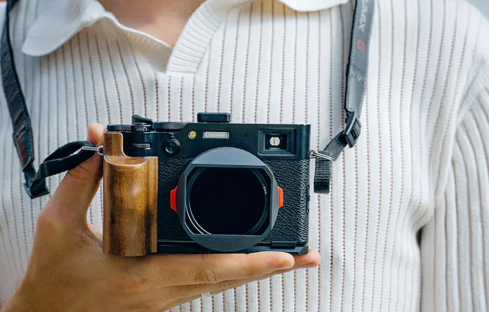 Camera with mounted grip hanging around the neck and held in hand.