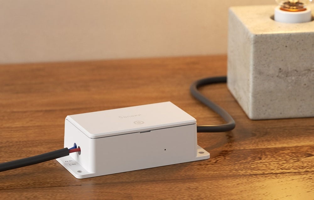 White smart relay Sonoff with connected wires on a wooden surface