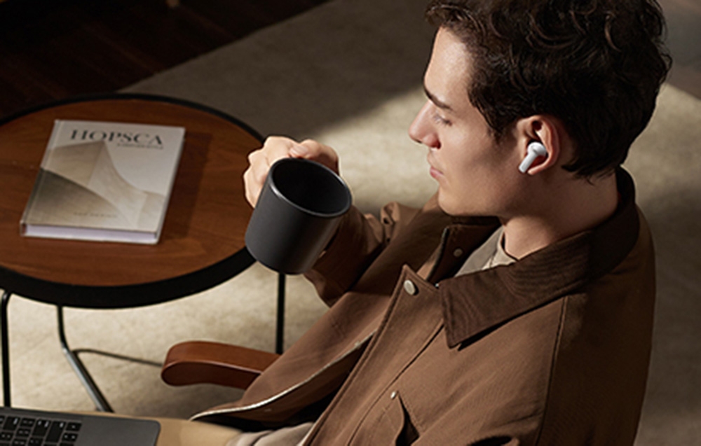 Mężczyzna z kubkiem kawy i białymi słuchawkami w uszach przy okrągłym stoliku