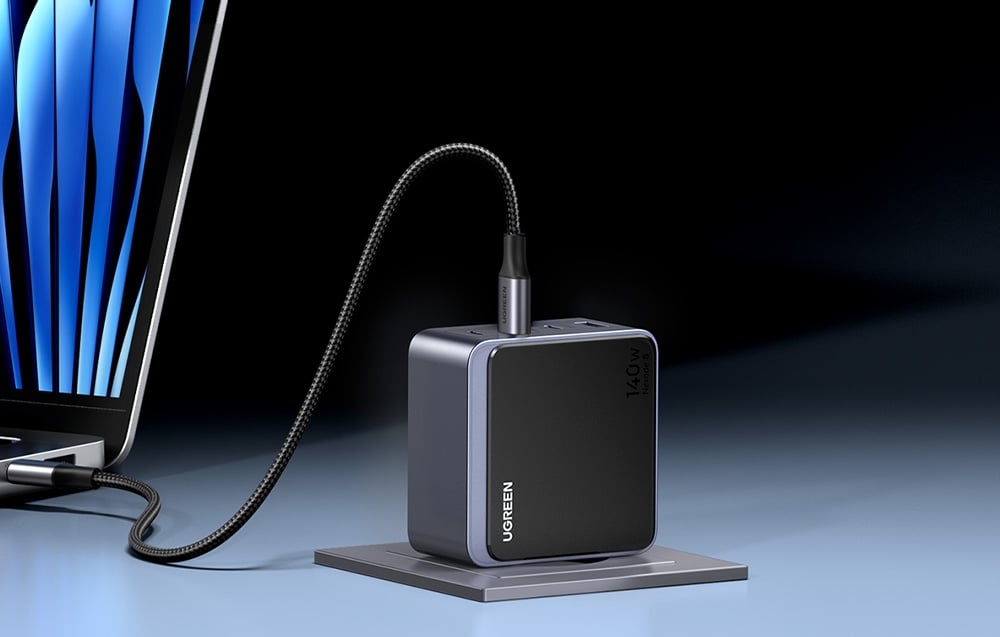 Ładowarka UGREEN Nexode S 140W podłączona do laptopa za pomocą przewodu USB-C, ustawiona pionowo na podstawce