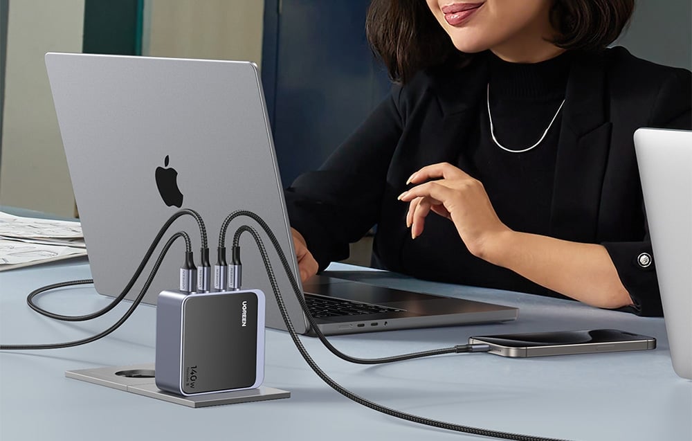 Kobieta pracująca przy laptopie Apple, do którego podłączona jest ładowarka UGREEN Nexode S 140W z czterema kablami USB