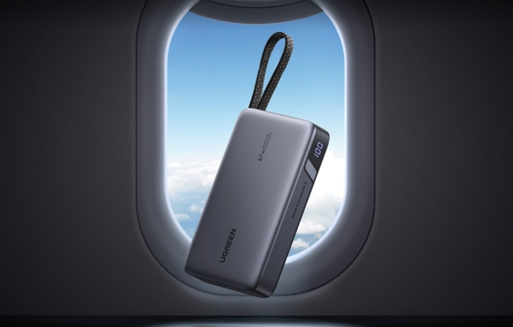 Graue Powerbank mit integriertem Kabel vor dem Fenster eines Flugzeugs