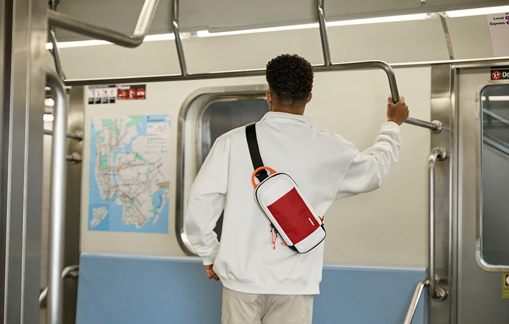 A man in a white jacket with a waist bag holding a handrail in a subway car with a map on the wall