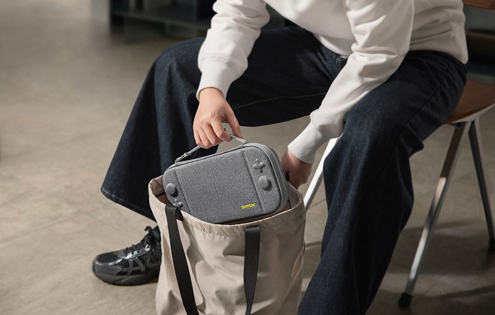 Person putting the gray console case into a beige shoulder bag