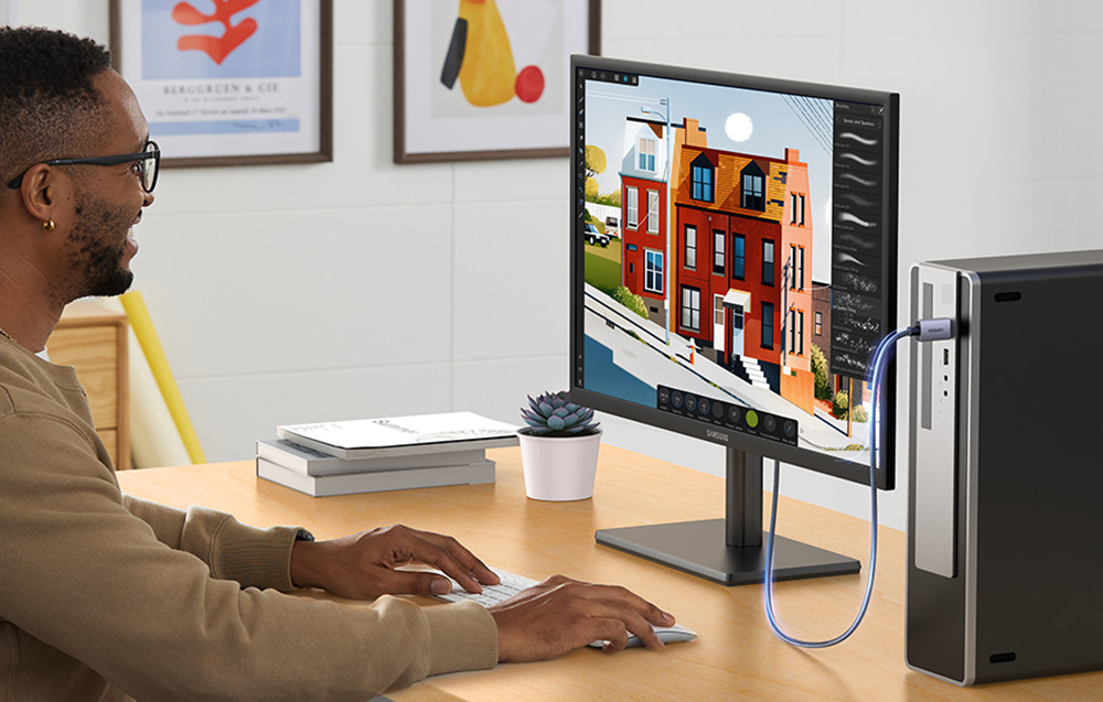 Mann arbeitet am Schreibtisch mit einem Monitor, der ein Grafikprogramm zeigt, daneben ein Desktop-Computer