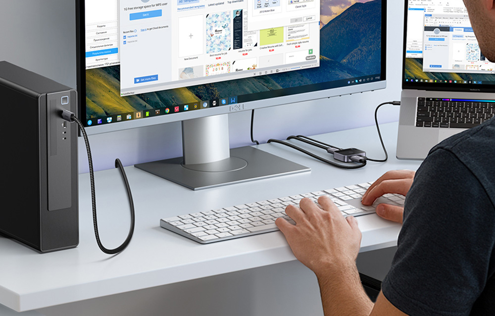 Eine Person arbeitet an einem Schreibtisch mit Monitor, Laptop, Tastatur und Maus, die mit dem Computer verbunden sind