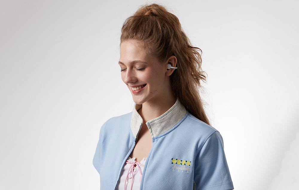 Uśmiechnięta kobieta w niebieskiej bluzie i ze słuchawkami bezprzewodowymi w uszach