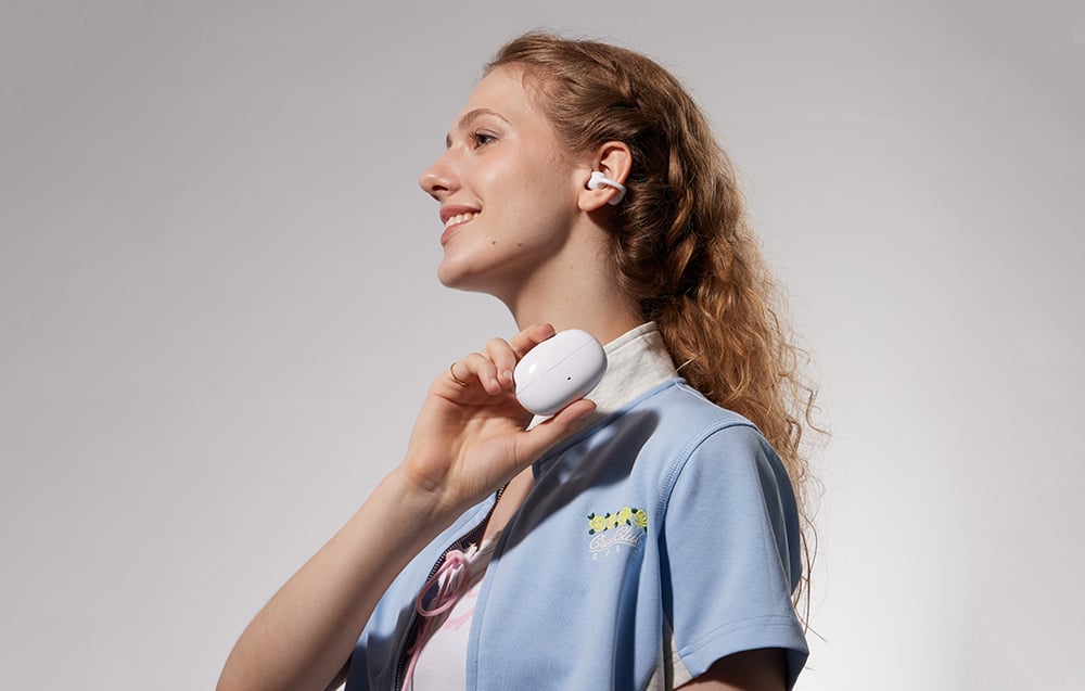 Kobieta z białymi słuchawkami trzyma przeznaczone dla nich etui ładujące na szarym tle