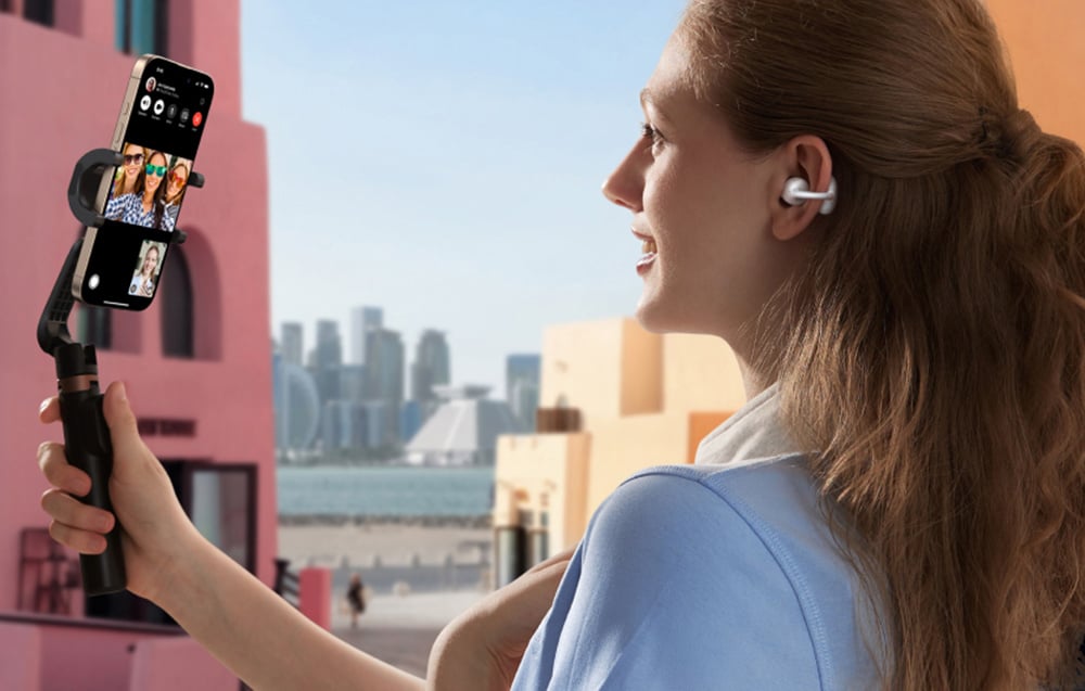 Kobieta trzyma gimbal ze smartfonem podczas wideorozmowy, nosząc słuchawki bezprzewodowe