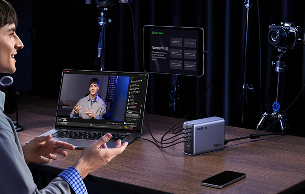 A person editing video on a laptop with a tablet, next to UGREEN charger and smartphone