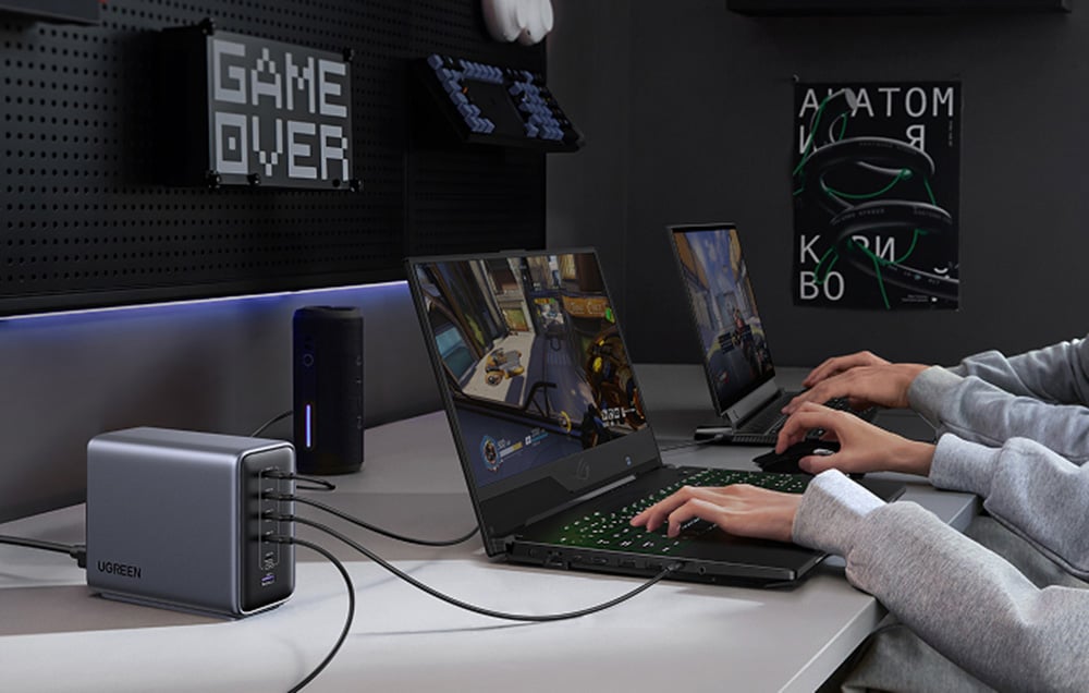 Two people playing on gaming laptops connected to the UGREEN charger on a desk