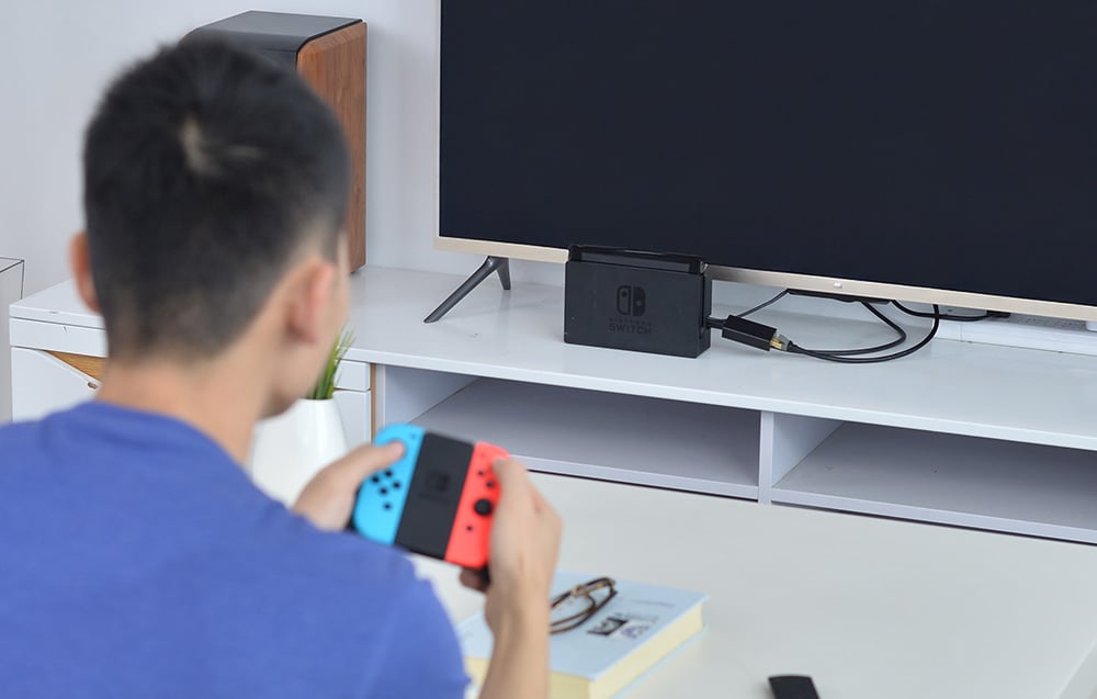A man playing on a Nintendo Switch console, standing on a shelf under the TV
